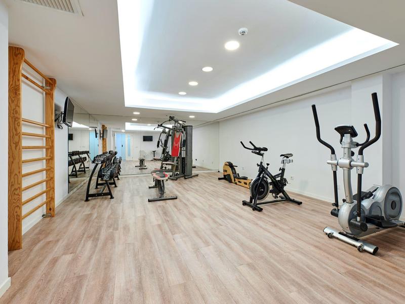 Nowoczesna siłownia z rowerami stacjonarnymi i maszynami do ćwiczeń na drewnianej podłodze i białych ścianach.