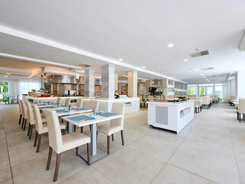 Przestronna nowoczesna jadalnia hotelowa z białymi krzesłami, stołami i bufetami.