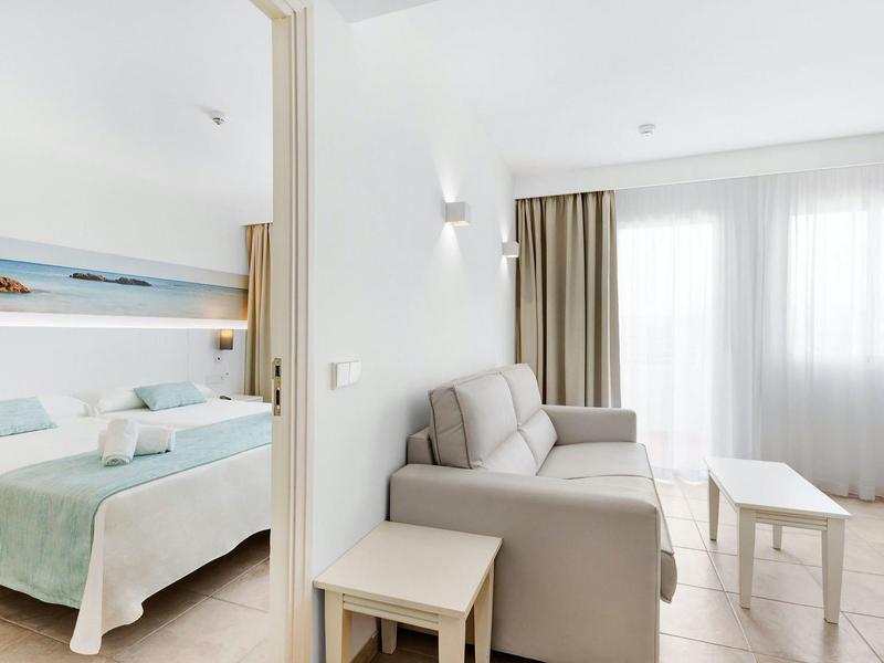 Jasny pokój hotelowy z dwoma łóżkami, sofą i dużym oknem z zasłonami.