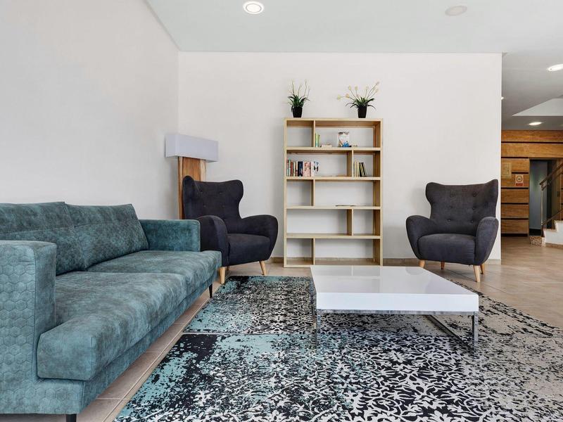 Nowoczesny salon z niebieską sofą, dwoma ciemnymi fotelami, białą półką i wzorzystym dywanem.