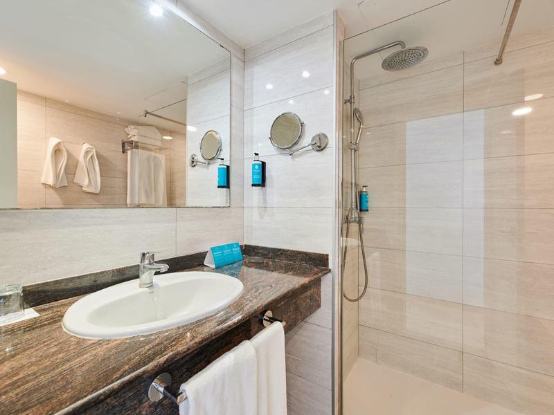 Nowoczesna łazienka z marmurowym blatem, umywalką, wieszakiem na ręczniki i szklaną kabiną prysznicową.