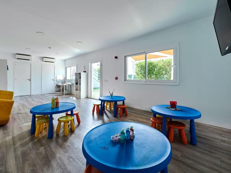 Jasny pokój zabaw z kolorowymi stolikami, małymi stołkami i telewizorem na ścianie w nowoczesnej przestrzeni.