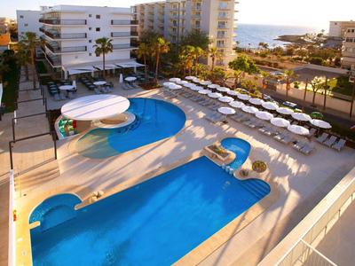 Basen hotelowy z leżakami i widokiem na morze o zachodzie słońca.