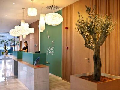 Nowoczesna recepcja hotelowa z zieloną ścianą, ladą i oświetleniem białymi lampami.