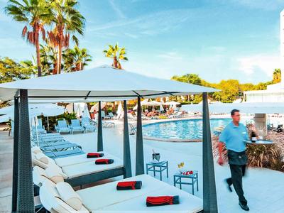 Lettini di lusso con asciugamani rossi sotto palme accanto a una piscina di un hotel.