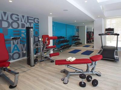 Nowoczesna siłownia z sprzętem i hantlami w jasnym pomieszczeniu.