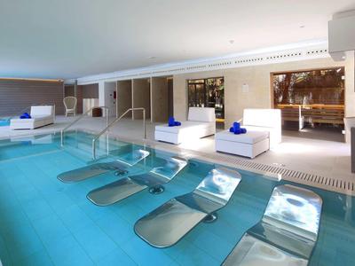 Nowoczesny basen hotelowy z wbudowanymi leżakami i białymi meblami przy basenie.