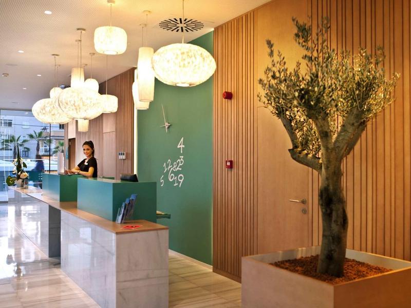 Nowoczesna recepcja hotelowa z zieloną ścianą, ladą i oświetleniem białymi lampami.