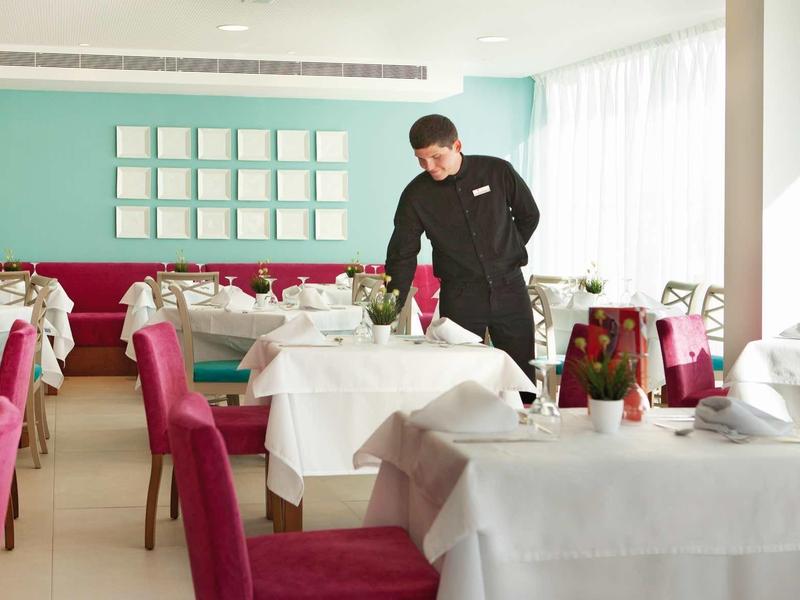 Kelner przygotowuje elegancko nakryte białe stoły z czerwonymi krzesłami w jasnej restauracji.