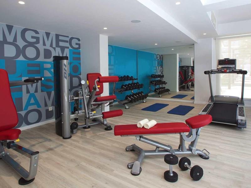 Nowoczesna siłownia z sprzętem i hantlami w jasnym pomieszczeniu.