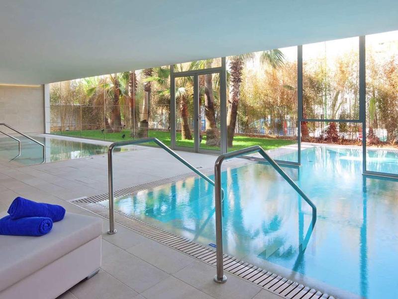 Basen kryty z leżakami i dużymi oknami z widokiem na drzewa na zewnątrz.