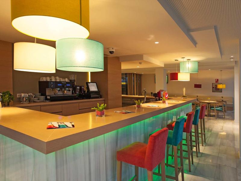 Nowoczesny bar hotelowy z kolorowymi stołkami i ciepłym oświetleniem.