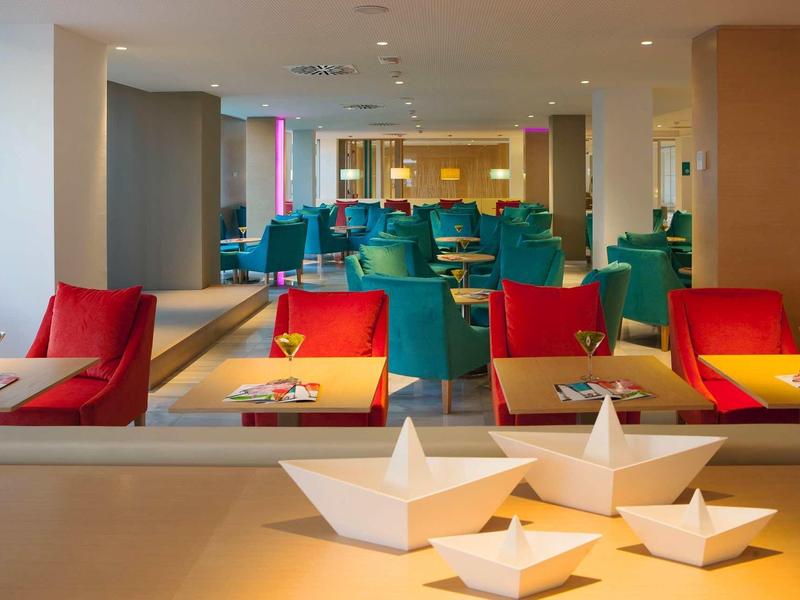 Nowoczesna strefa wypoczynkowa w hotelu z kolorowymi fotelami i ozdobnymi papierowymi łódkami.