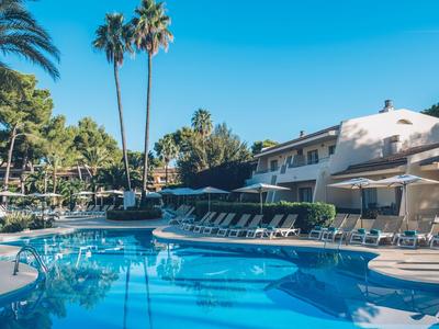 Ein Hotelpool mit Liegestühlen, Palmen und klarem blauem Himmel im Hintergrund.