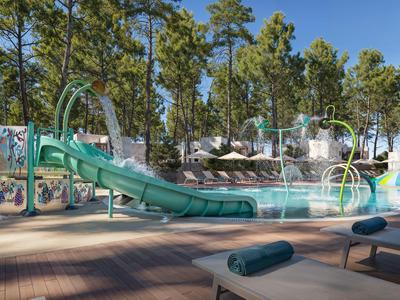 Wasserpark mit Rutschen, Planschbecken und schattigen Sitzbereichen, umgeben von Bäumen.
