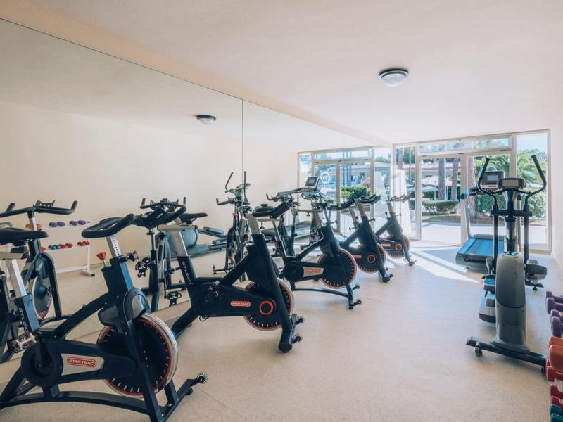 Jasna siłownia z wieloma rowerkami spinningowymi i sprzętem przy dużych oknach.
