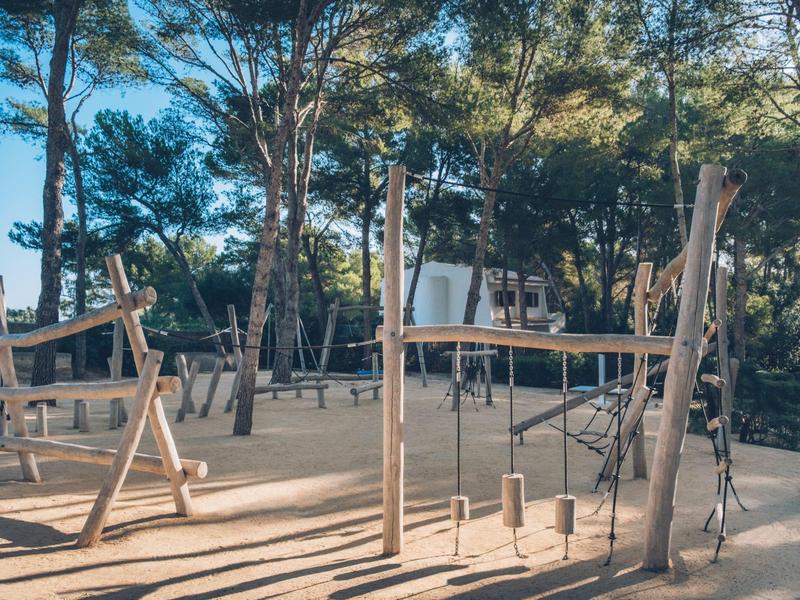Drewniany plac zabaw na świeżym powietrzu z huśtawkami i konstrukcjami do wspinaczki wśród drzew.