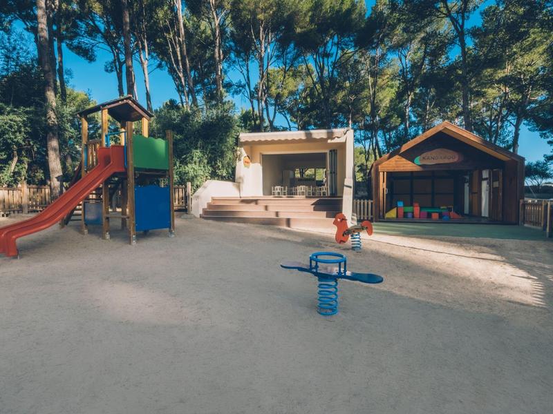 Plac zabaw dla dzieci ze zjeżdżalnią i wahadłem przed domkami letniskowymi na terenie leśnym.