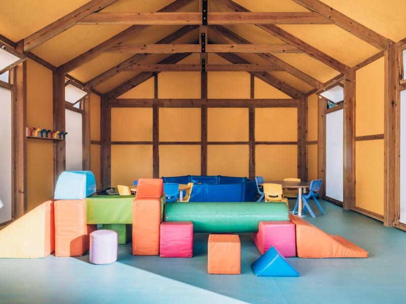 Kolorowe poduszki i maty dla dzieci w jasnym pokoju z drewnianymi belkami.