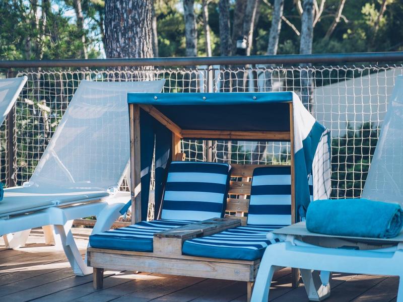 Wygodne niebieskie leżaki i kabina plażowa przy basenie z drzewami w tle.