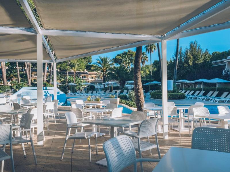 Nowoczesny, słoneczny taras na zewnątrz z białymi stołami i krzesłami obok basenu i palm.