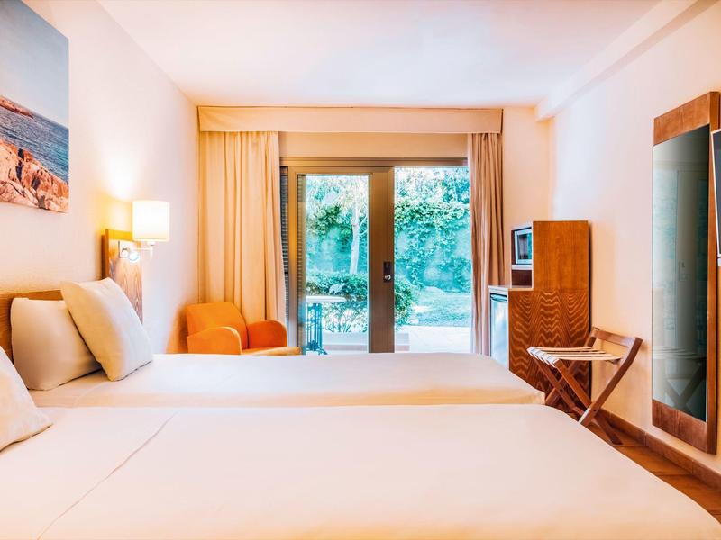 Jasny pokój hotelowy z dwoma łóżkami i drzwiami na taras z widokiem na ogród