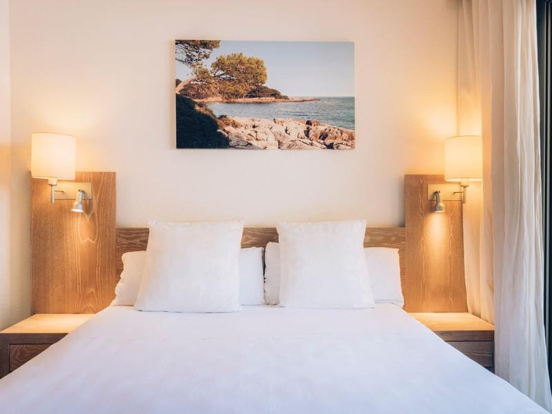 Jasne łóżko podwójne z białymi poduszkami i minimalistyczną dekoracją w pokoju hotelowym.