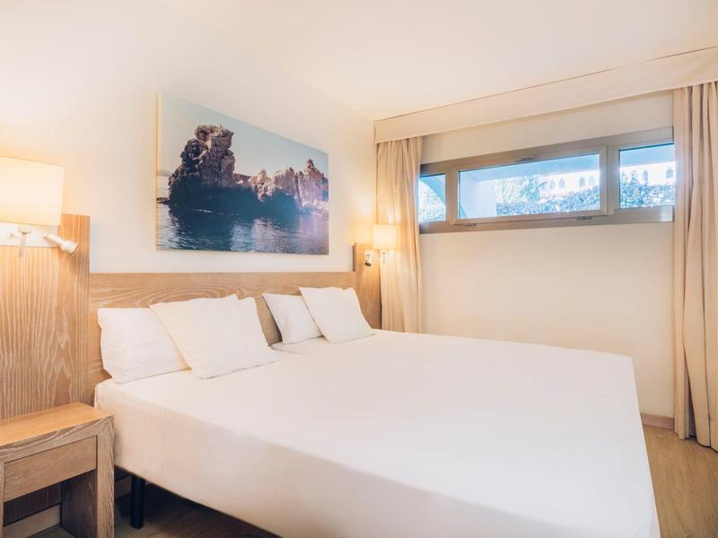 Jasny pokój hotelowy z dużym łóżkiem, drewnianymi meblami i obrazem krajobrazu.