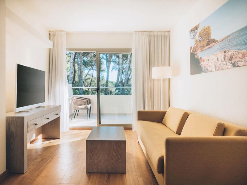 Jasny salon z brązową sofą, telewizorem i balkonem z widokiem na palmy i morze.