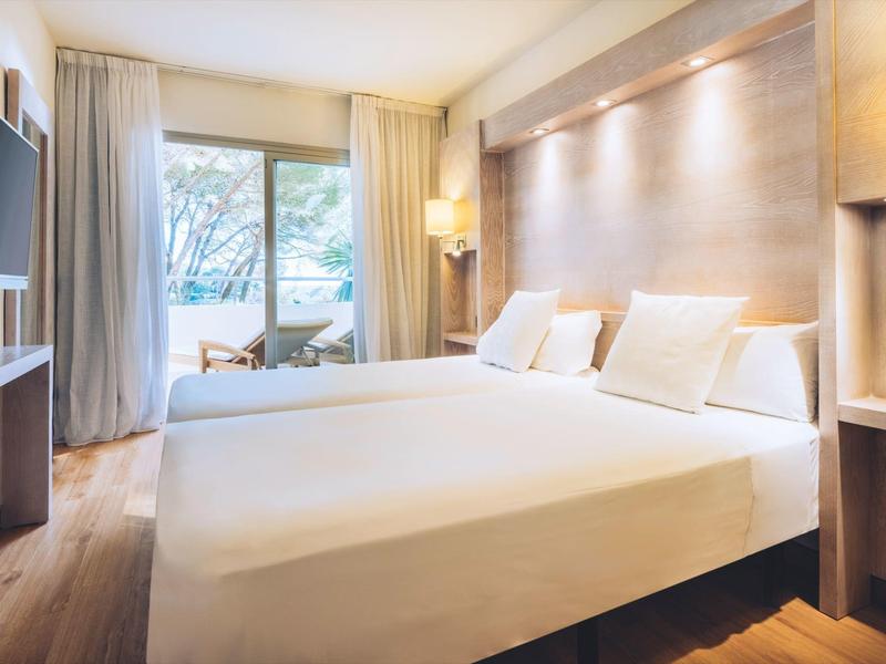 Nowoczesny pokój hotelowy z dużym łóżkiem, telewizorem, szafą i oknem z widokiem na zewnątrz.