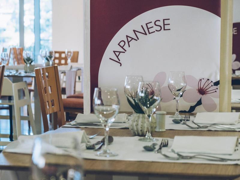 Elegancka restauracja z nakrytymi stołami, kieliszkami do wina i ścianą z napisem „Japanese”.
