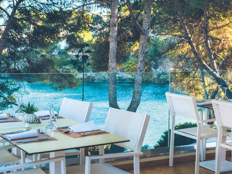 Taras z białymi krzesłami i stołami z widokiem na zalesione jezioro.