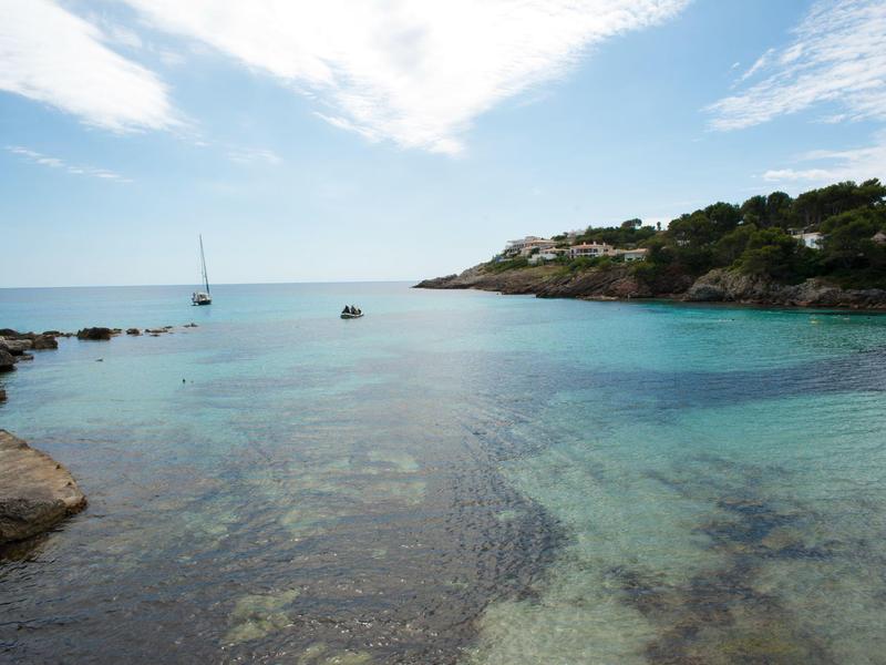 Czysta woda morska z żaglówką i skalistym wybrzeżem w tle.