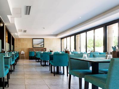 Ristorante moderno con sedie turchesi e grandi finestre che lasciano entrare molta luce naturale.