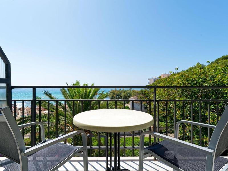 Balcone con due sedie e un piccolo tavolo rotondo con vista su palme e mare.