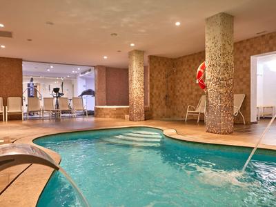 Indoor pool with warm water, seating area, and large windows in a wellness area.