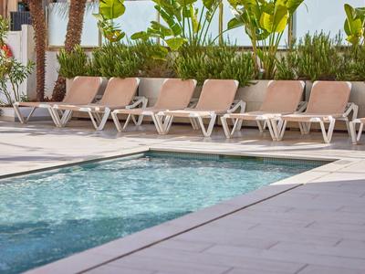 Bazén s lehátky a zelenými rostlinami v pozadí za denního světla.