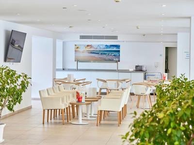 Bright, modern café with white chairs, tables, and plants indoors.