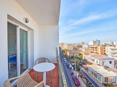 Balcony with table and chairs overlooking a city street and blue sky.