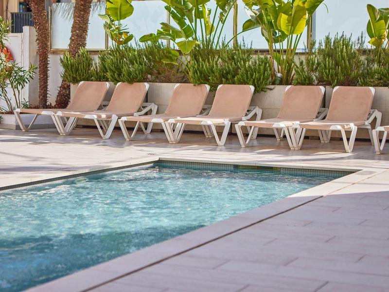 Swimming pool with clear water and lounge chairs beside it in a hotel setting.