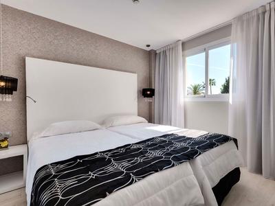 Modernes Schlafzimmer mit Doppelbett, weißem Kopfteil, grauer Tapete und großem Fenster mit Vorhängen.