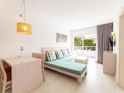 Minimalistische hotelkamer met tweepersoonsbed, bureau en balkon met uitzicht op groen.