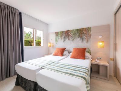 Modern hotelkamer met twee eenpersoonsbedden, oranje kussens en een groot raam.