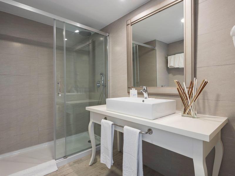 Nowoczesna łazienka z umywalką, lustrem, szklaną kabiną prysznicową i ręcznikami.