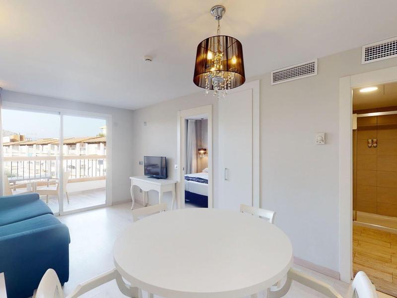 Jasny salon z niebieską sofą, stołem jadalnym oraz dostępem do balkonu i łazienki.