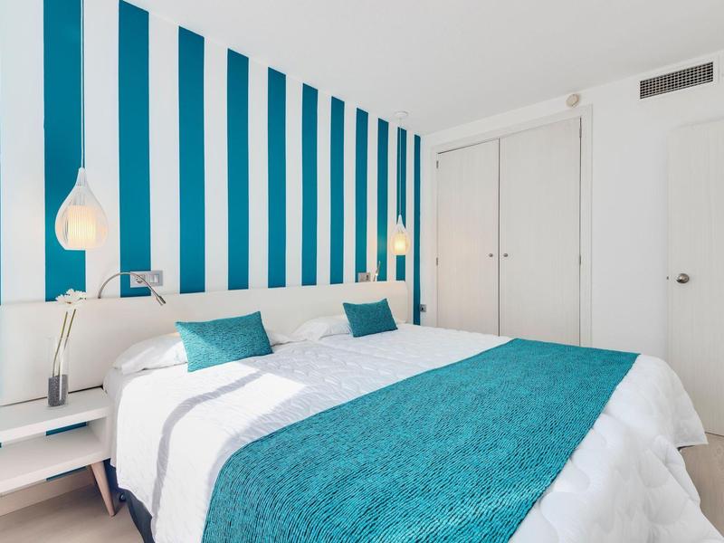 Jasny pokój z ścianą w niebiesko-białe pasy i łóżkiem podwójnym z turkusowymi akcentami.