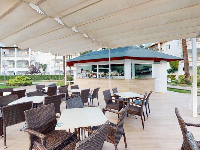Zewnętrzny obszar z miejscami do siedzenia z krzesłami i stołami pod markizą obok budynku.