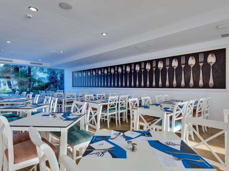 Nowoczesna jadalnia z białymi stołami i dekoracyjną ścianą z motywem sztućców.