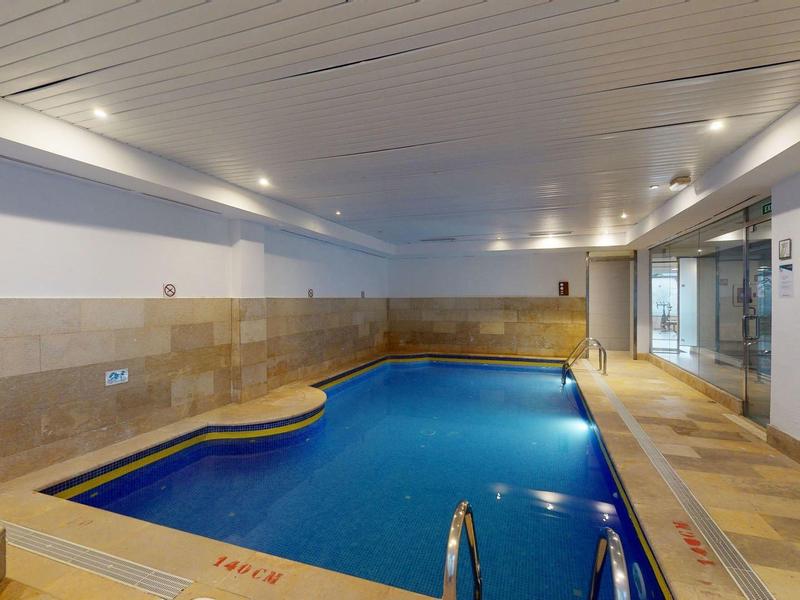 Ogrzewany basen kryty z czystą niebieską wodą i beżowymi płytkami w hotelu.