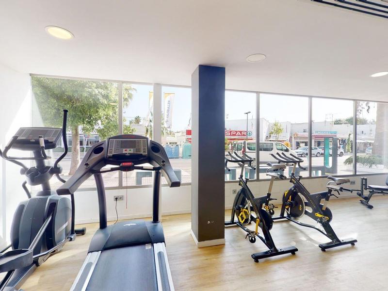 Jasna siłownia z nowoczesnym sprzętem i dużymi oknami z widokiem na taras.
